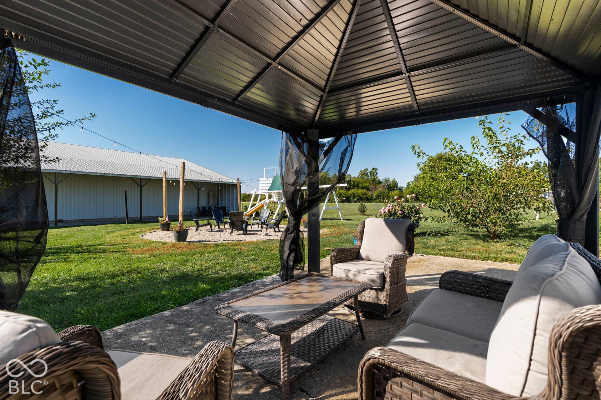 Concrete patio with a metal gazebo, screened sides, and an expansive lawn