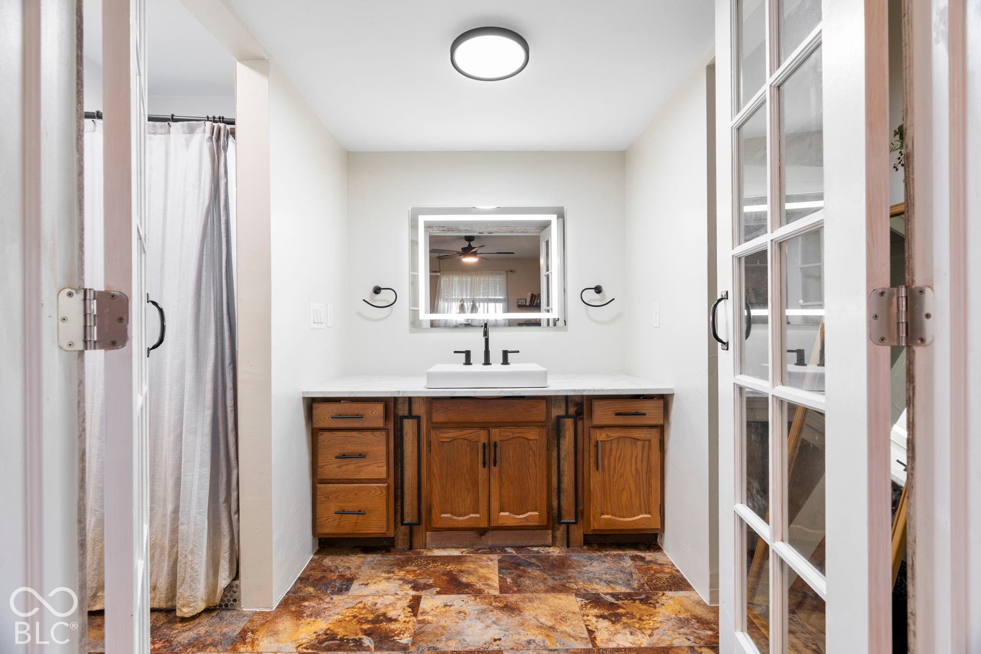 Spa-inspired primary bathroom featuring custom wood cabinetry with ample storage, dual vanity with white countertop and polished chrome fixtures, large framed mirror with integrated lighting, heated tile flooring, and recessed ceiling lighting