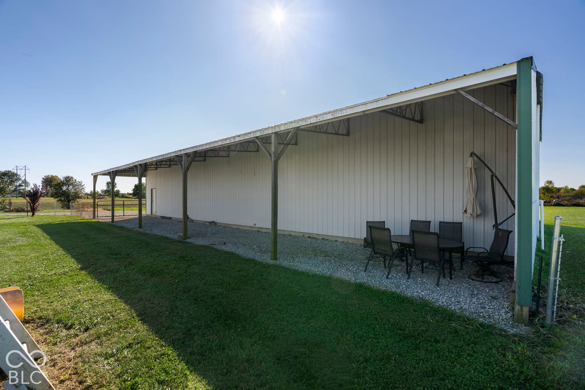 Spacious covered pavilion with metal roof and support posts, featuring a gravel base and expansive lawn