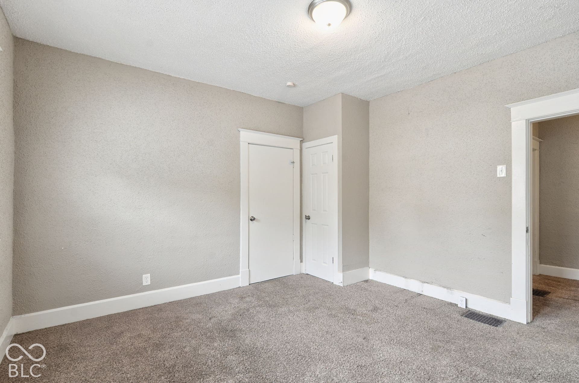 Neutral-toned carpet flooring with textured walls, white trim, and a flush mount ceiling light