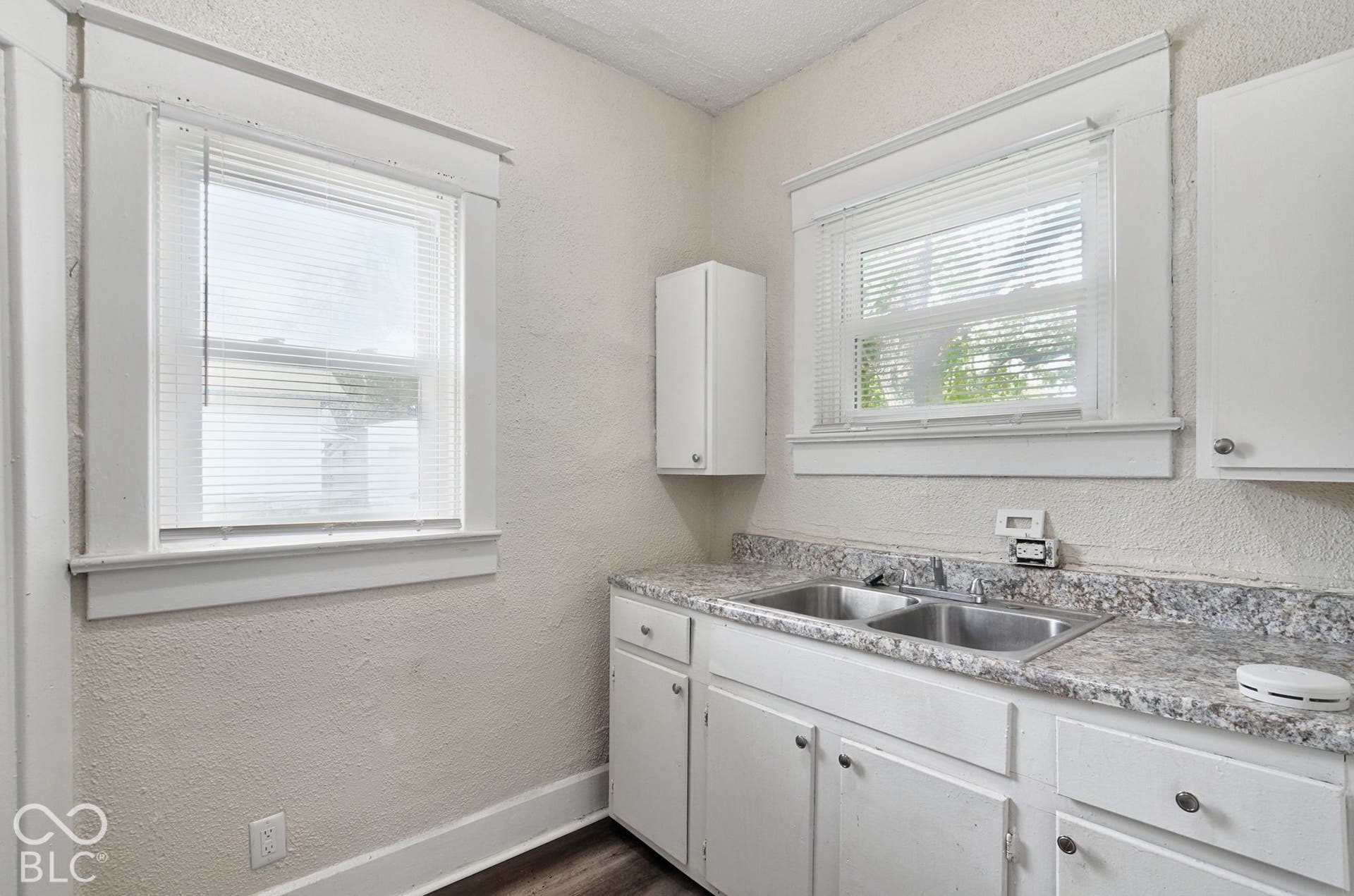 White cabinetry with stainless steel hardware, dual basin stainless steel sink, and speckled countertop
