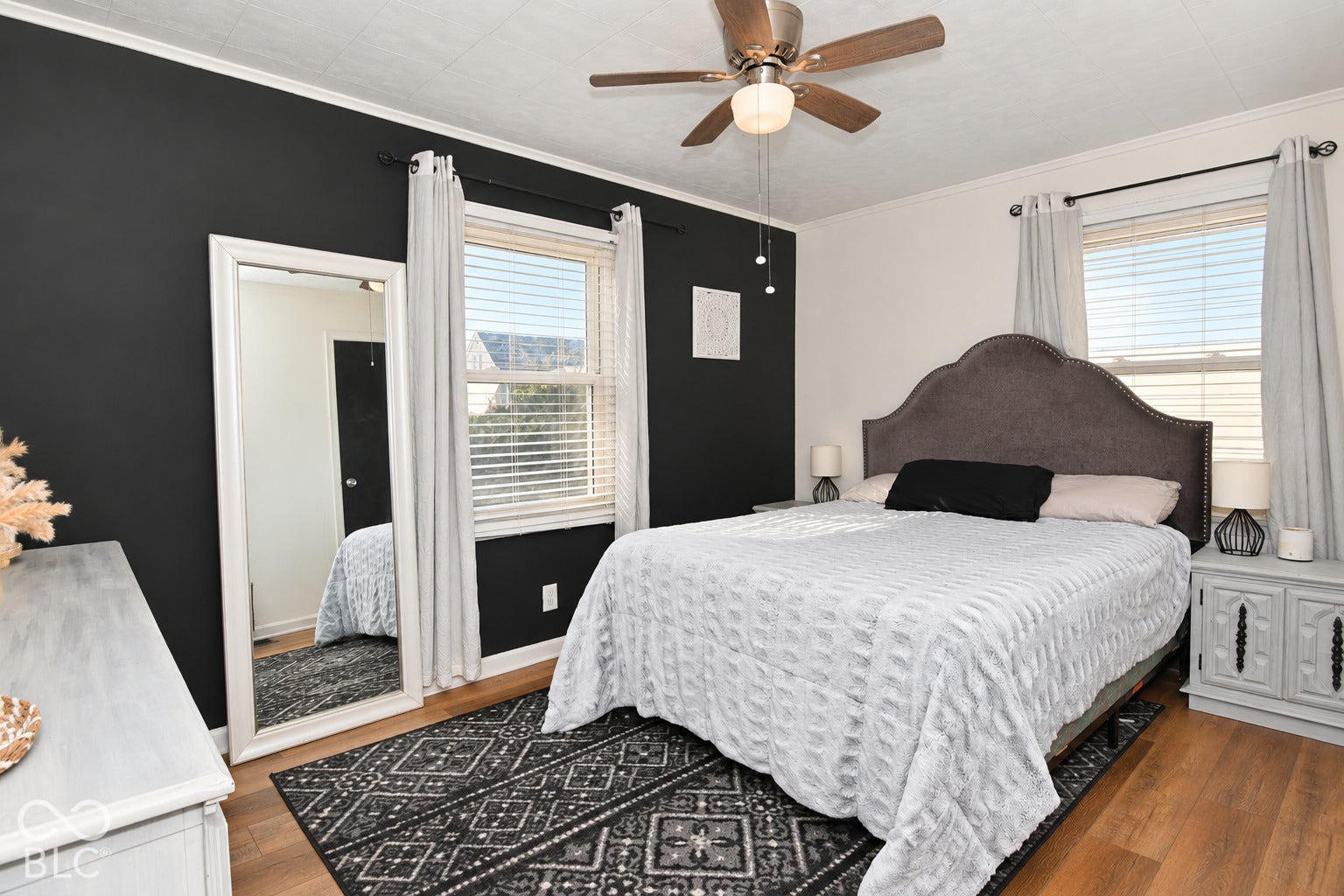 Wood-finish flooring with white baseboards, featuring a window with blinds and drapes, and a ceiling fan with integrated lighting