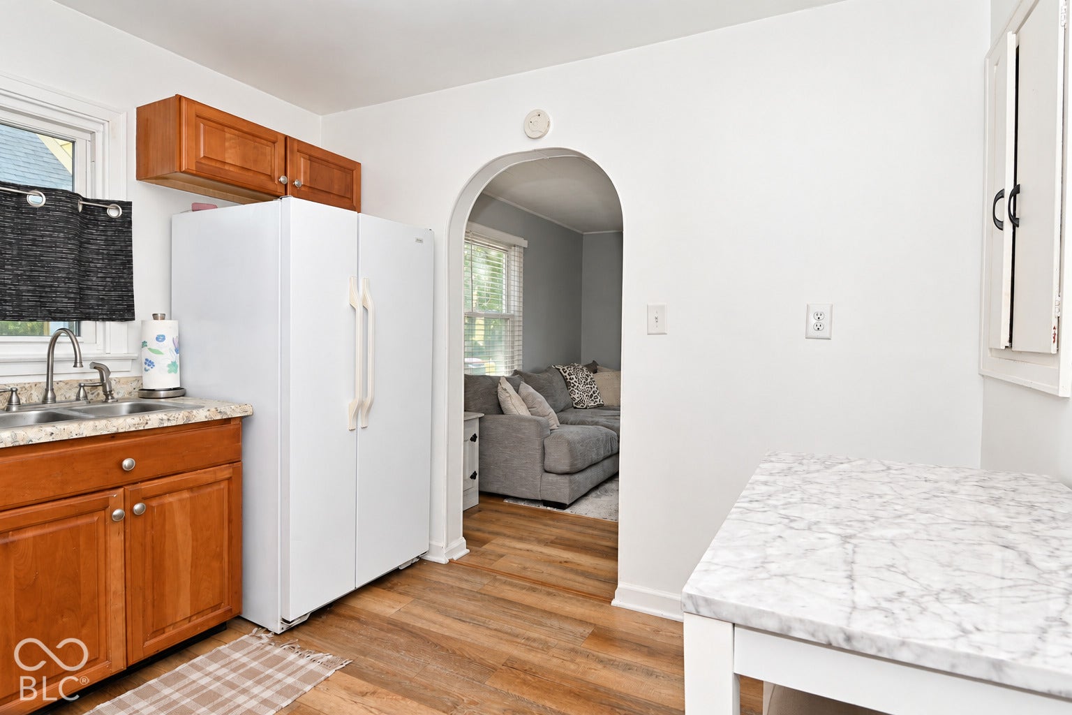 Open kitchen and dining area featuring wood cabinetry, white refrigerator, marble-finish countertops, wood-finish flooring, and an arched passageway providing access to additional living spaces