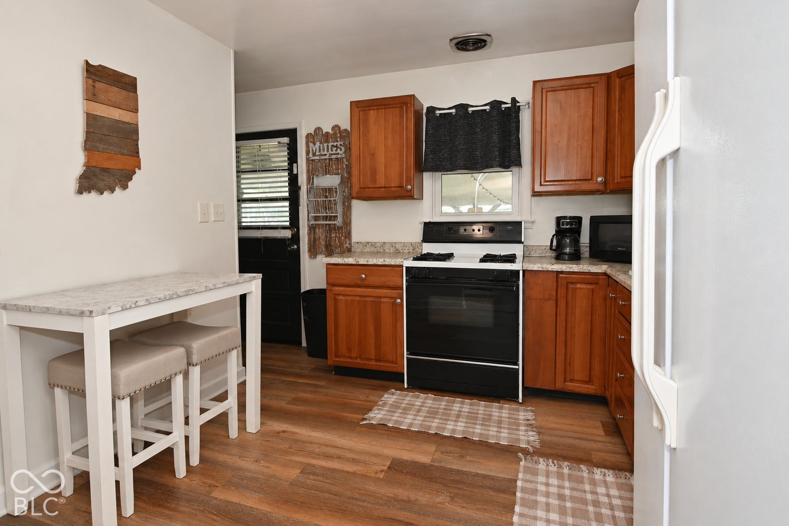 Wood-finish flooring with solid wood cabinetry, a white stone-finish countertop, and a black range