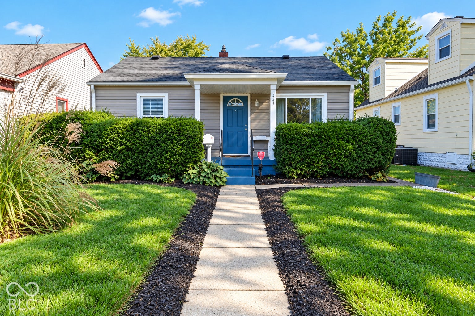 Charming cottage-style home featuring a manicured front lawn with ornamental grasses, defined mulch landscaping borders, and mature hedges flanking the entrance