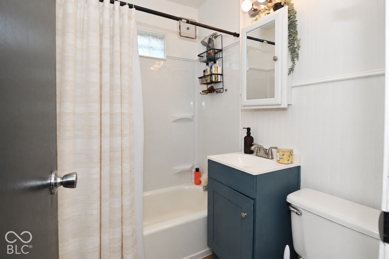 White paneled wall detailing, white vanity with integrated sink, white medicine cabinet with mirrored door, chrome faucet, and white bathtub with shower