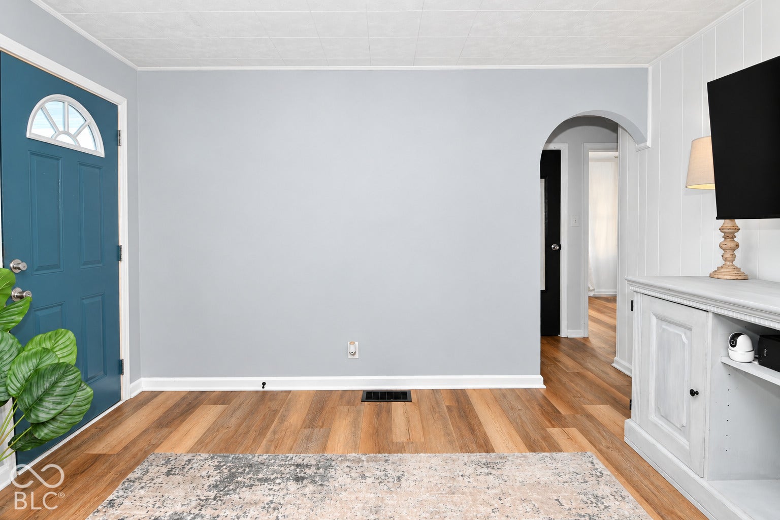 Wood-finish flooring, light gray wall paint, arched doorway, paneled accent wall, and a solid blue entry door with a decorative transom window