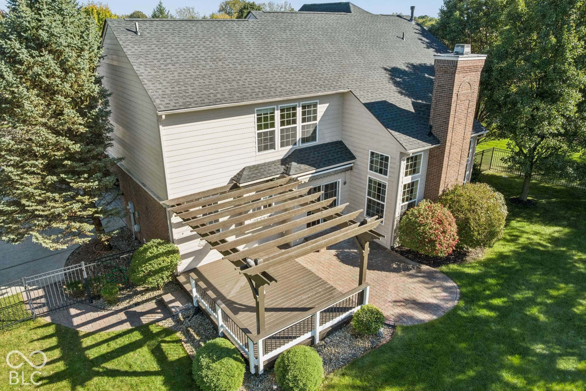 Aerial view showcases the home's expansive paver patio, pergola, mature landscaping and backyard setting.