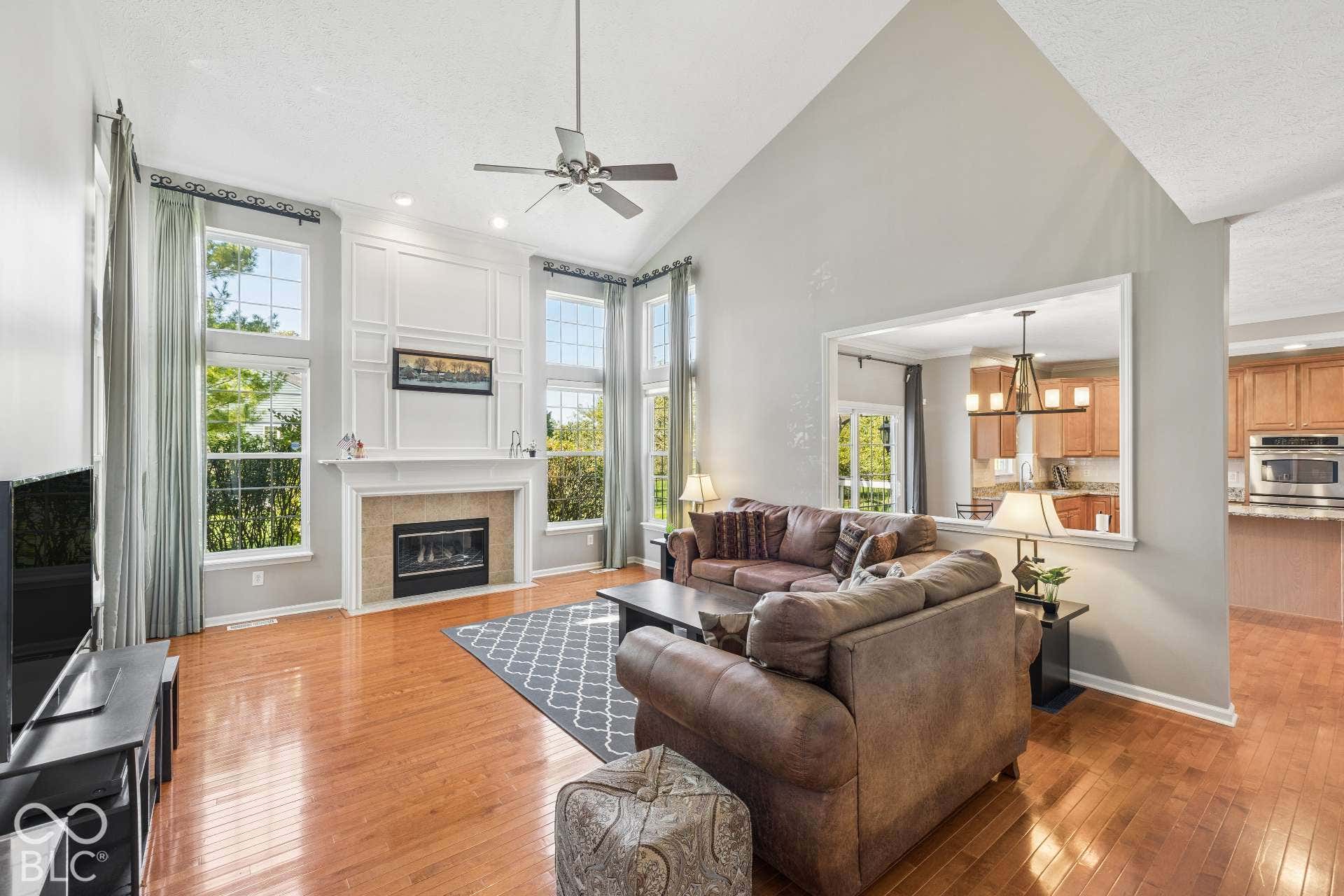 A second view highlights the impressive ceiling height, fireplace, natural light and open connection to the kitchen.