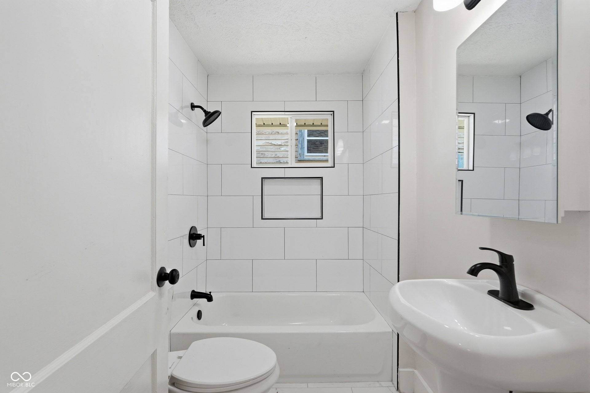 Bathroom featuring a pedestal sink, white subway tile shower surround, built-in shower niche, and matte black fixtures