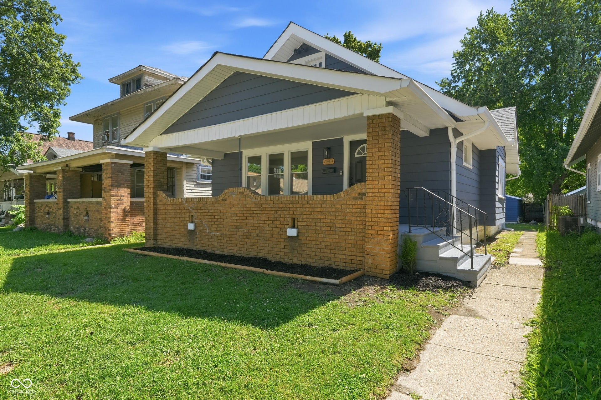 Craftsman-style home featuring a covered front porch with brick pillars and a half-wall, grey siding, white trim, and a concrete walkway