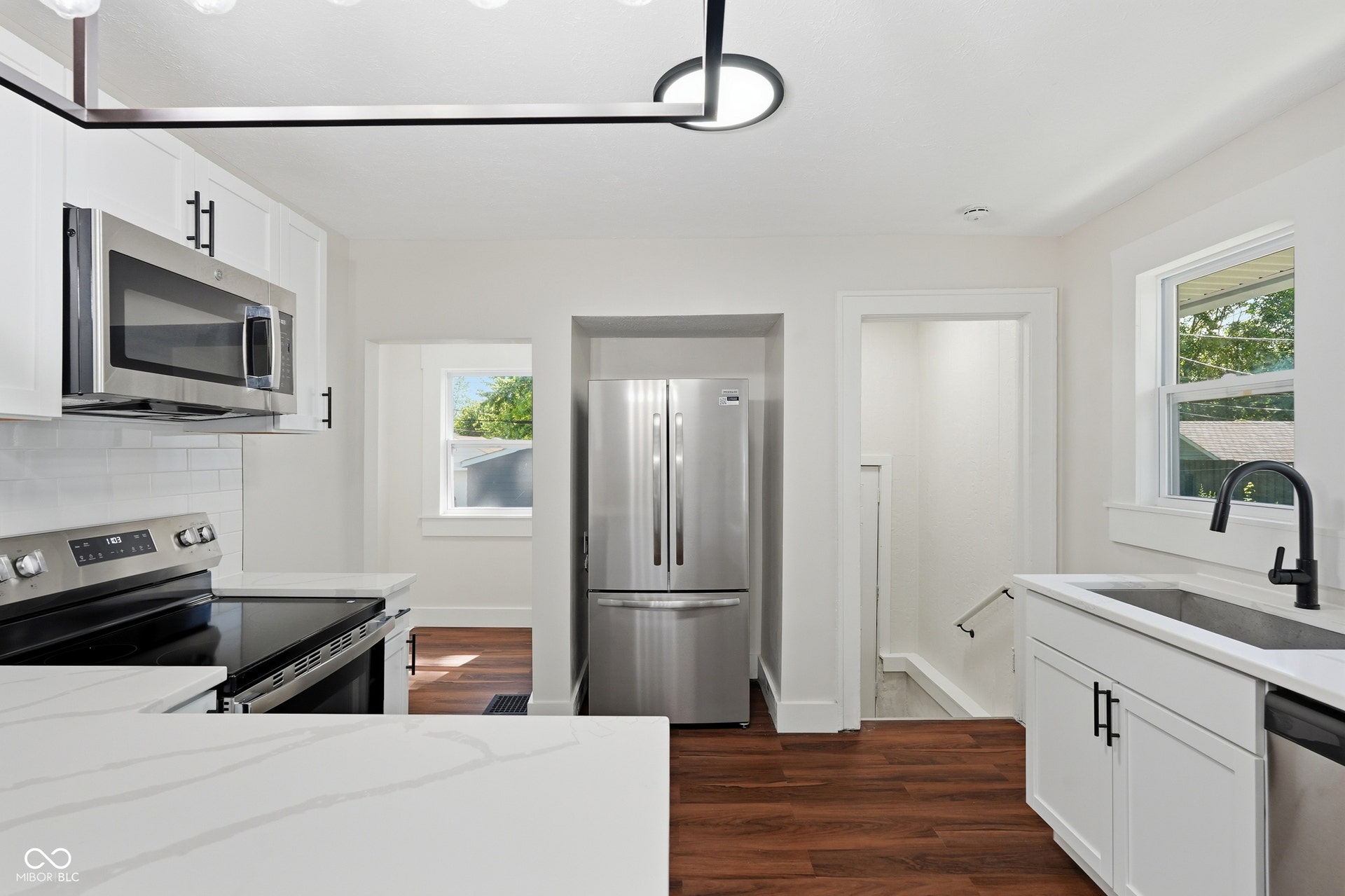 Renovated kitchen featuring white cabinetry, stainless steel appliances, quartz countertops, a subway tile backsplash, and wood-finish flooring