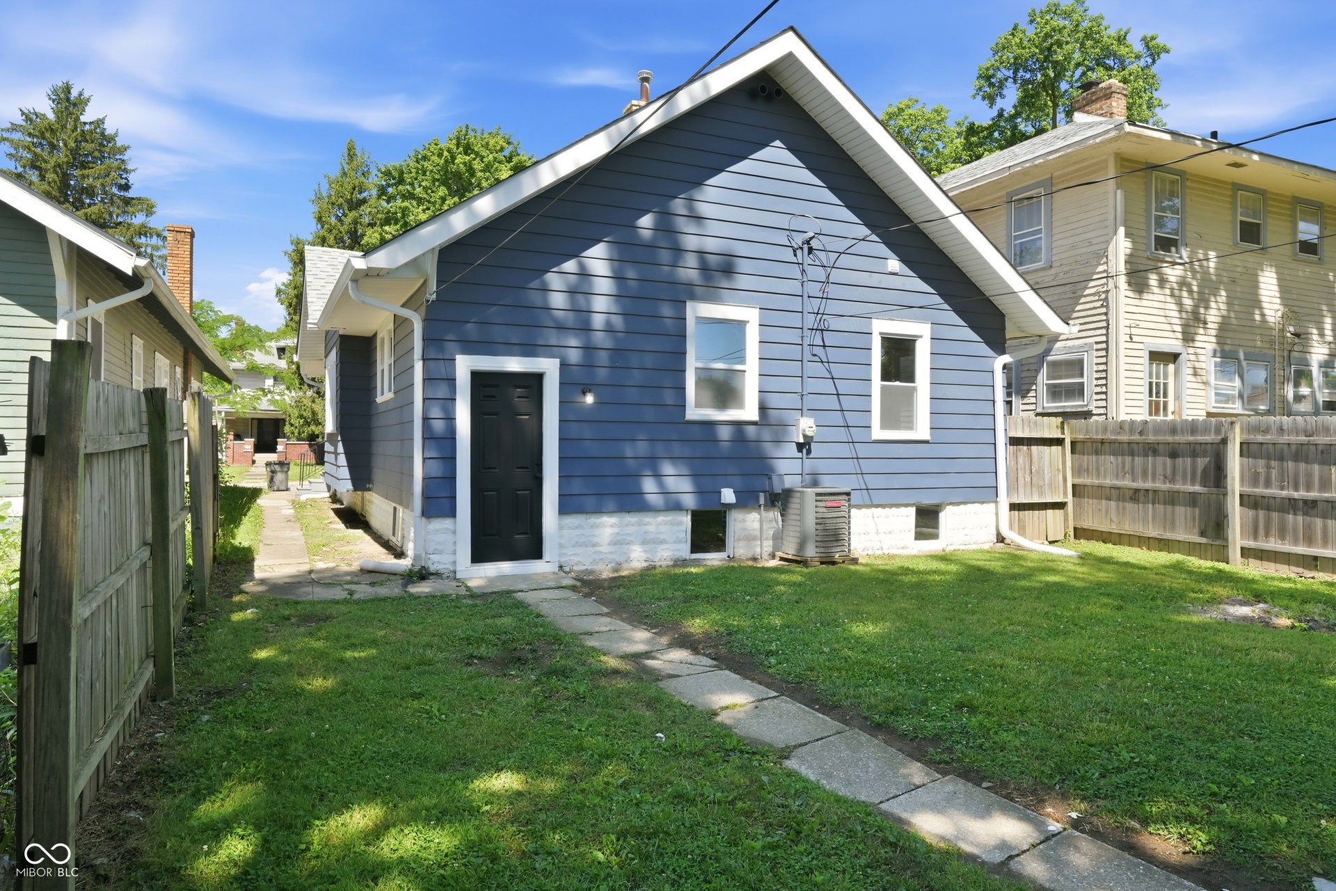 Rear exterior with blue siding, white trim, a black door, and a concrete paver pathway