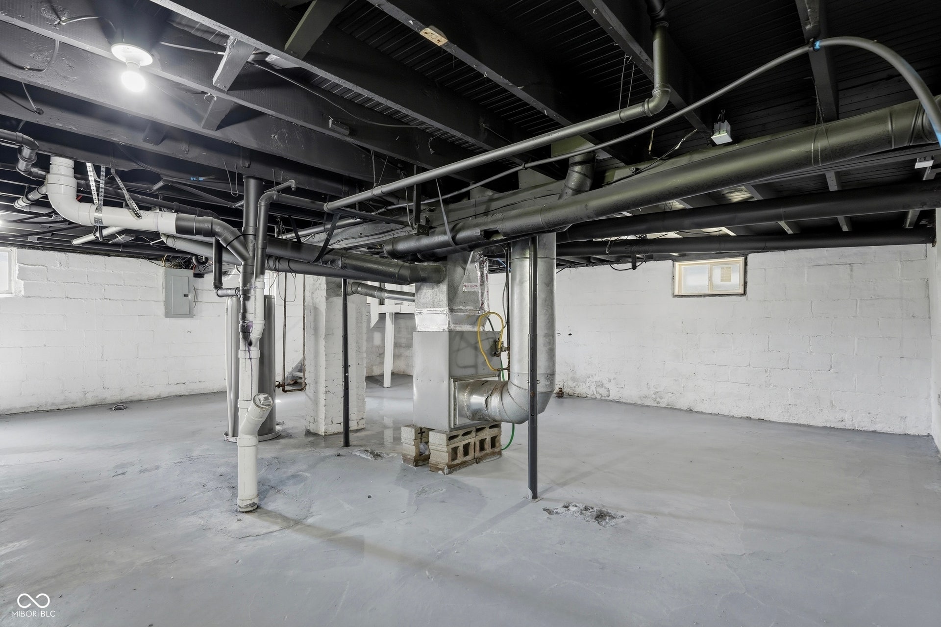 Spacious unfinished basement featuring exposed overhead piping and ductwork, white painted brick walls, and concrete flooring