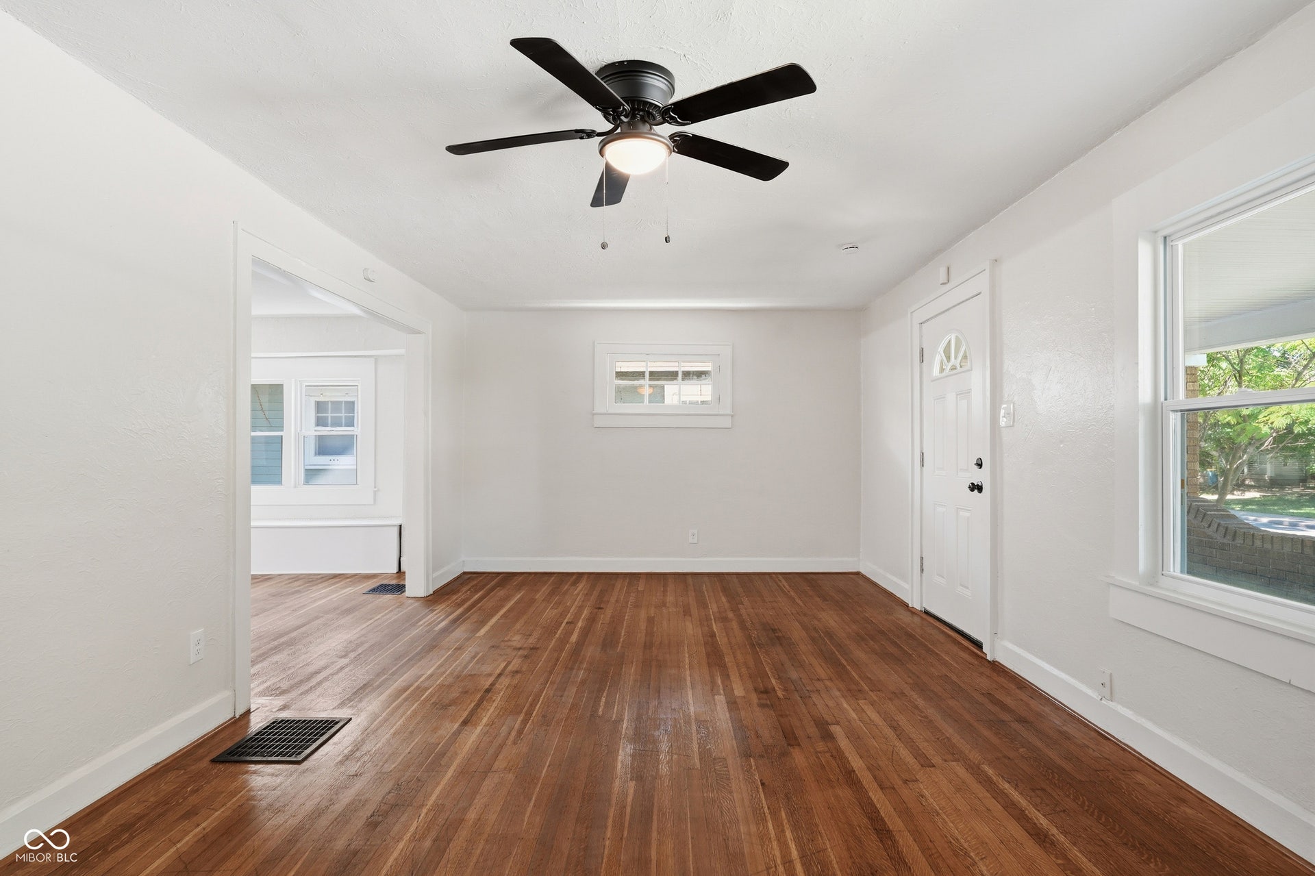 Spacious interior featuring wood-finish flooring, a contemporary ceiling fan with integrated lighting, and multiple windows providing natural illumination
