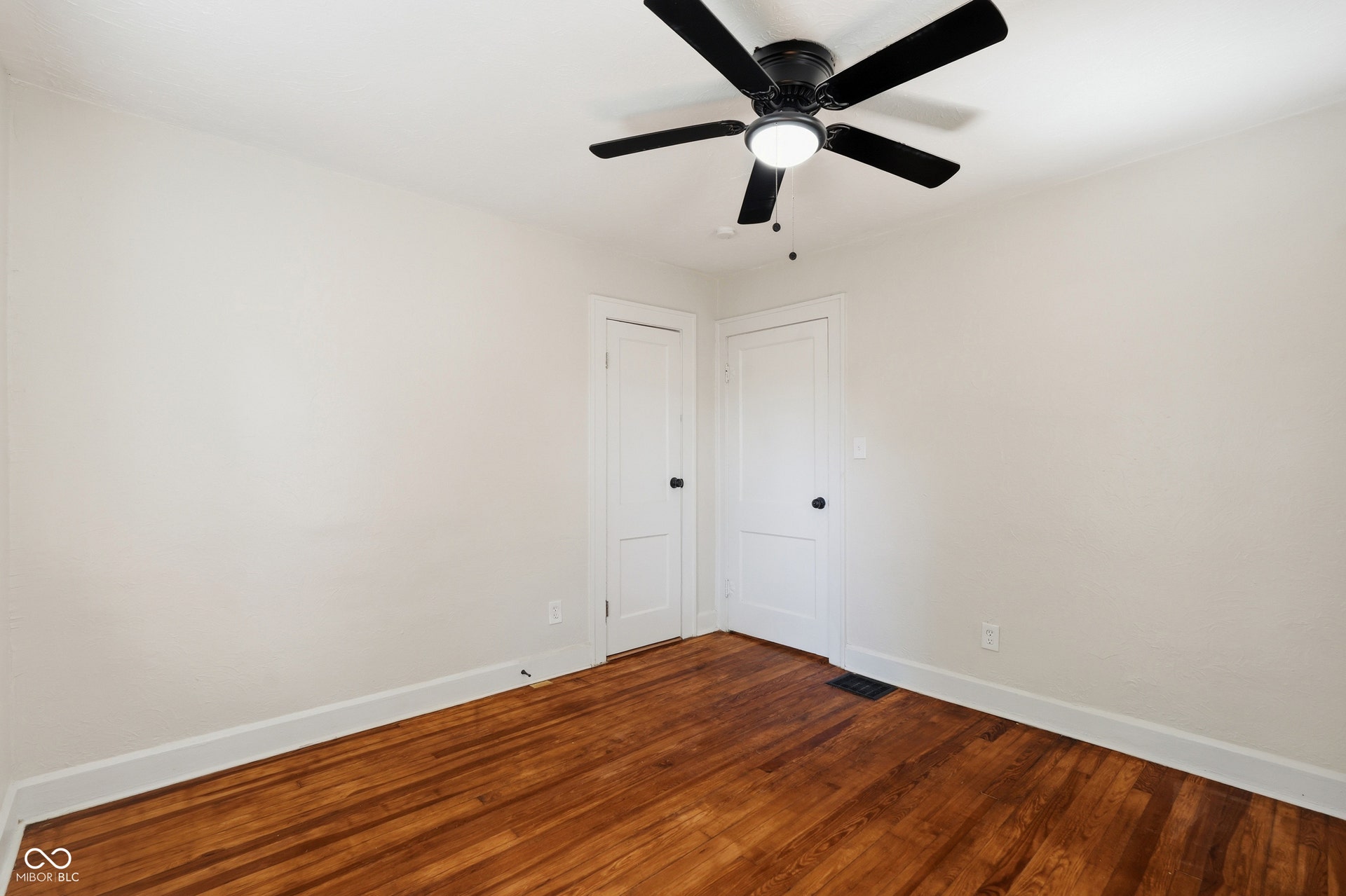 Spacious room featuring wood flooring, white painted walls, and white baseboards