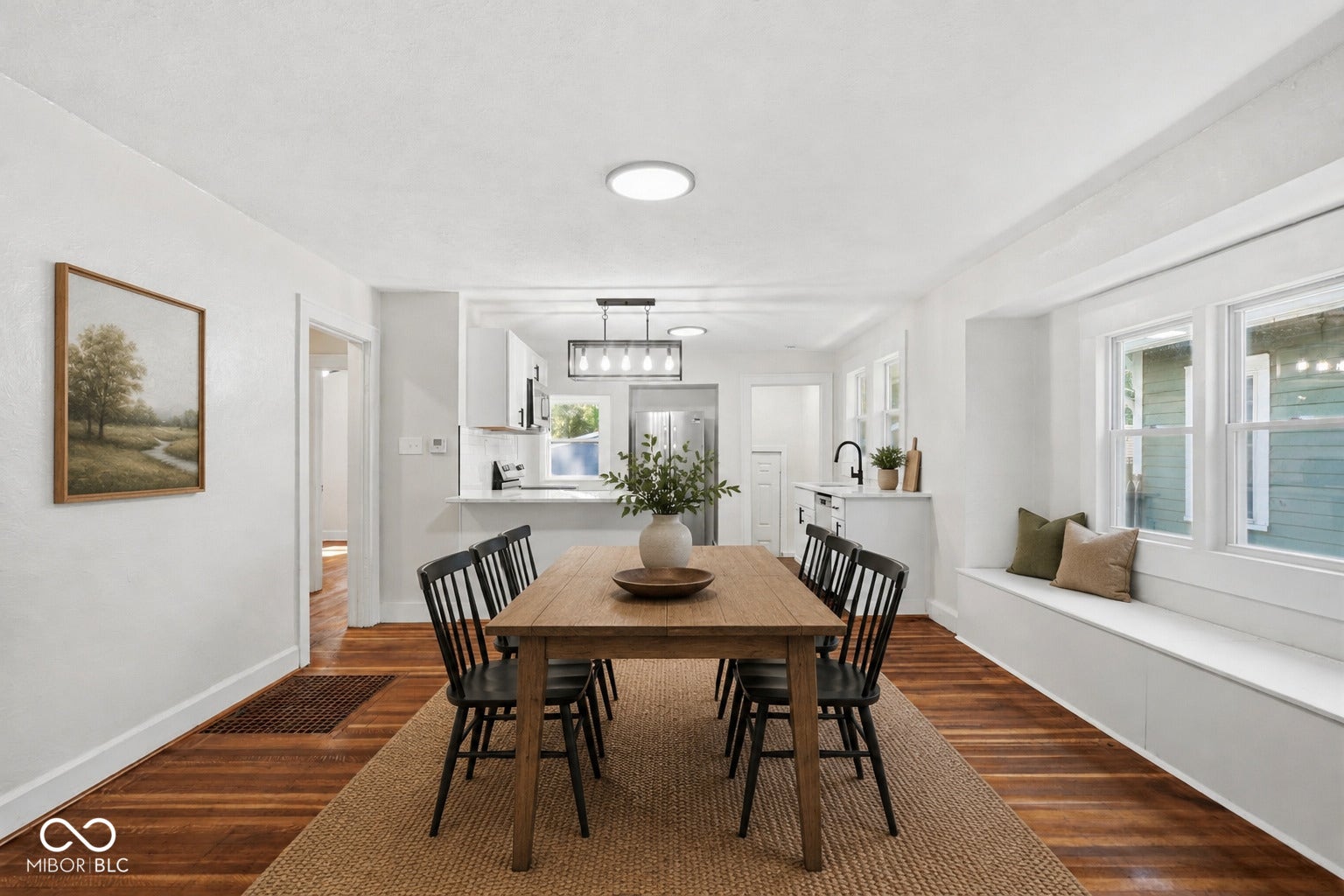 Virtually Altered - Dining area featuring wood-finish flooring, a built-in window bench, recessed lighting, and a partial view into the kitchen with white cabinetry and a breakfast bar - **VIRTUALLY STAGED**