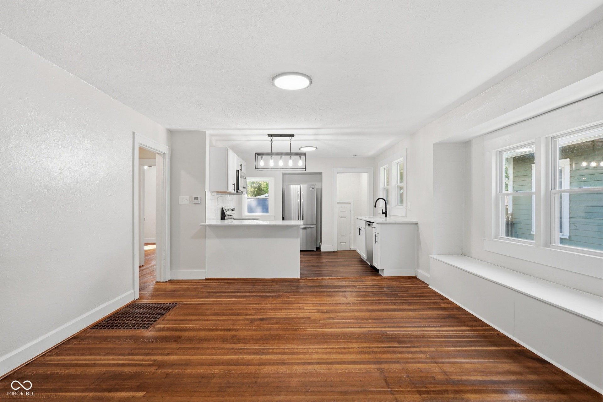 Bright open-concept living area with wood-finish flooring, recessed lighting, and a built-in window bench