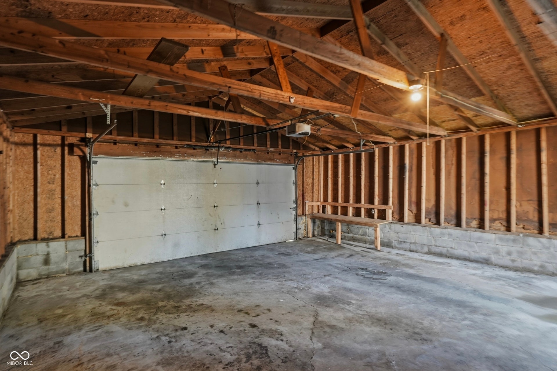 Attached garage featuring a concrete floor, exposed wood framing, a built-in wood bench, and a single ceiling light fixture