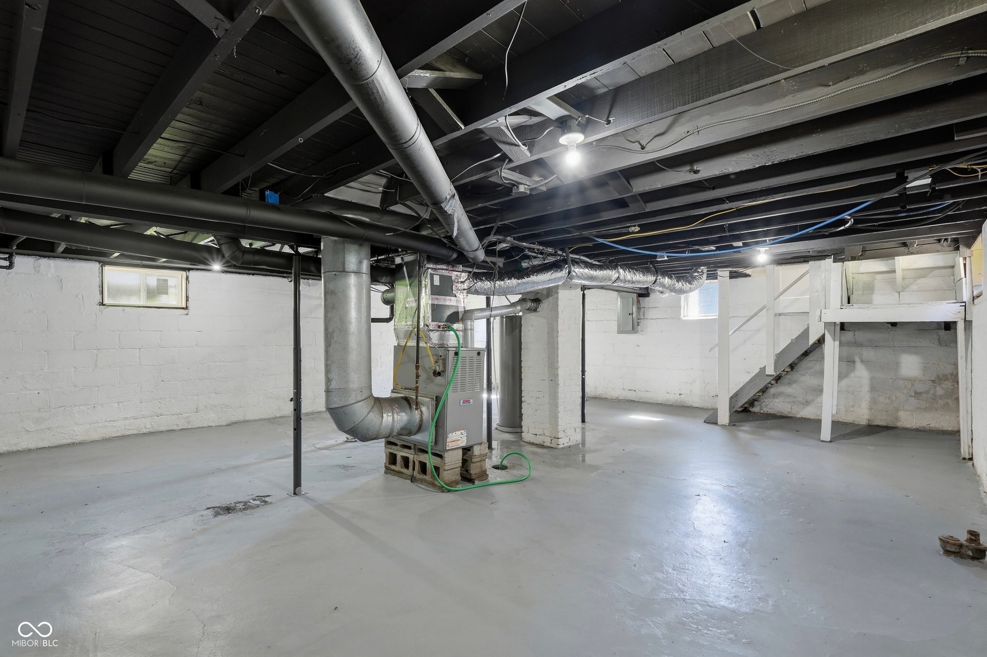 Expansive unfinished basement featuring painted concrete block walls, painted concrete flooring, exposed overhead joists, and a utility furnace system