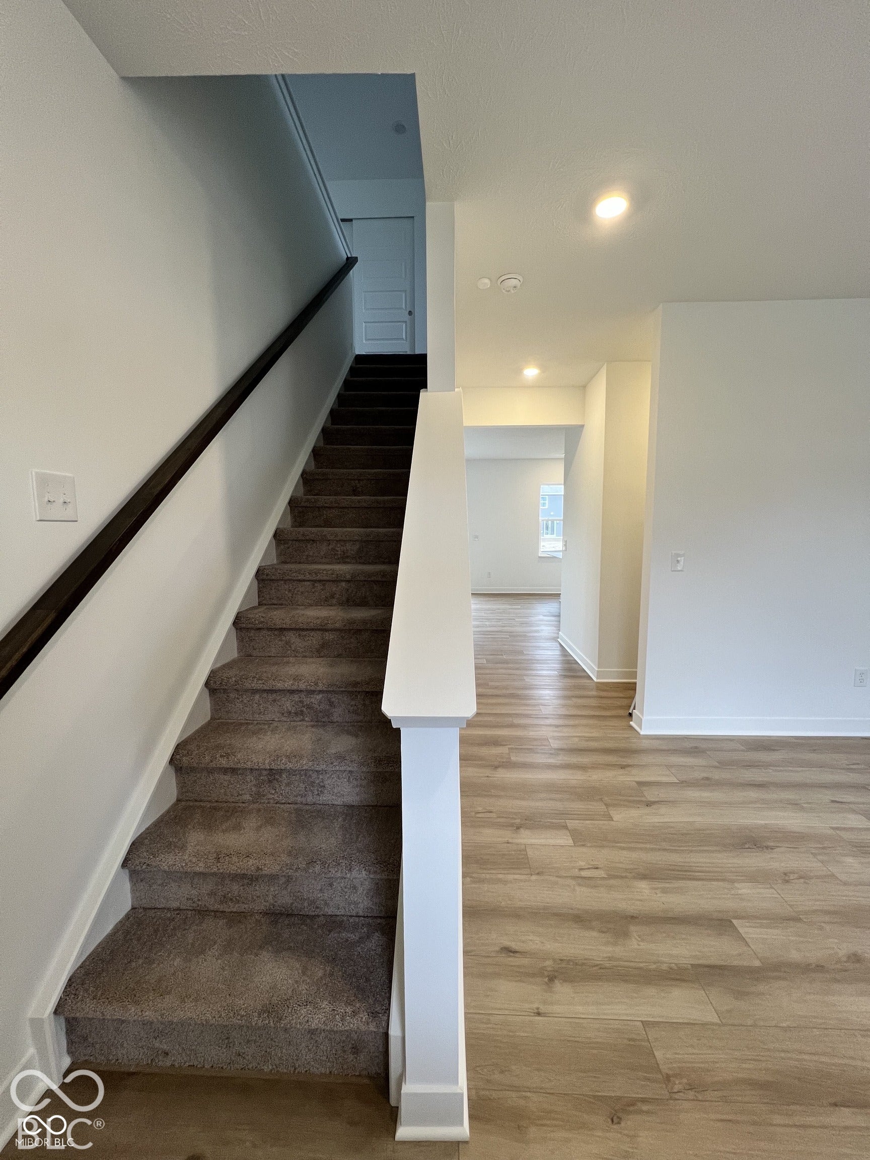 Carpeted staircase with dark wood-finish handrail, white baluster, and wood-finish flooring