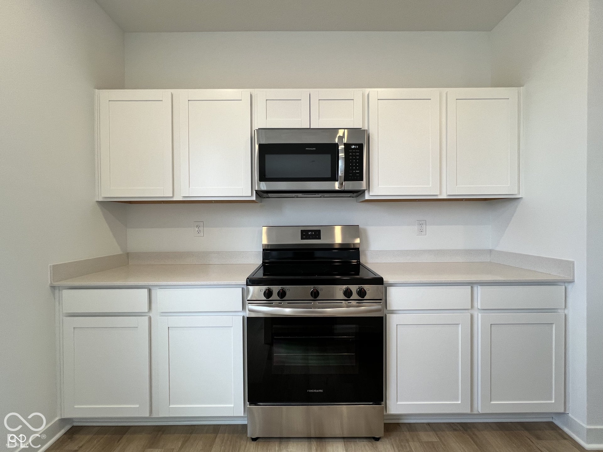 White shaker-style cabinetry, light-toned countertops, stainless steel microwave, stainless steel range, wood-finish flooring