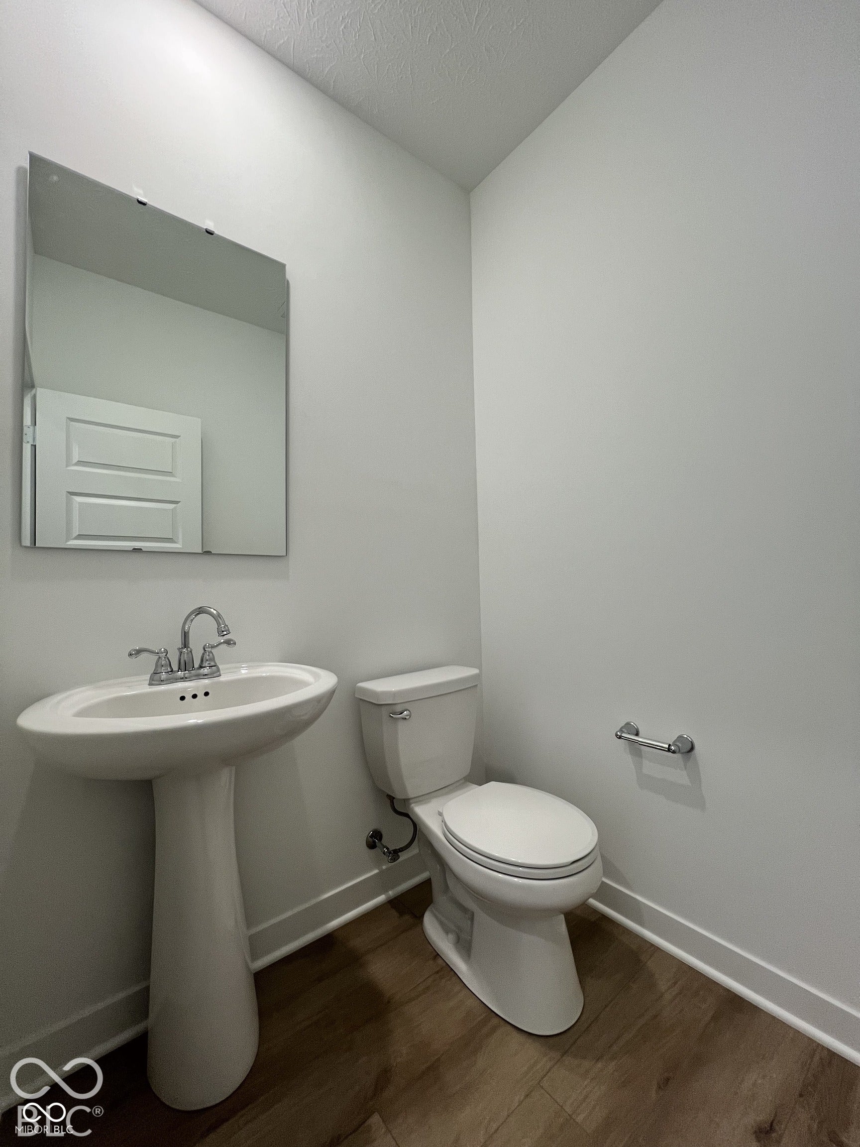 Pedestal sink with chrome faucet, wall-mounted mirror, toilet, and wood-finish flooring