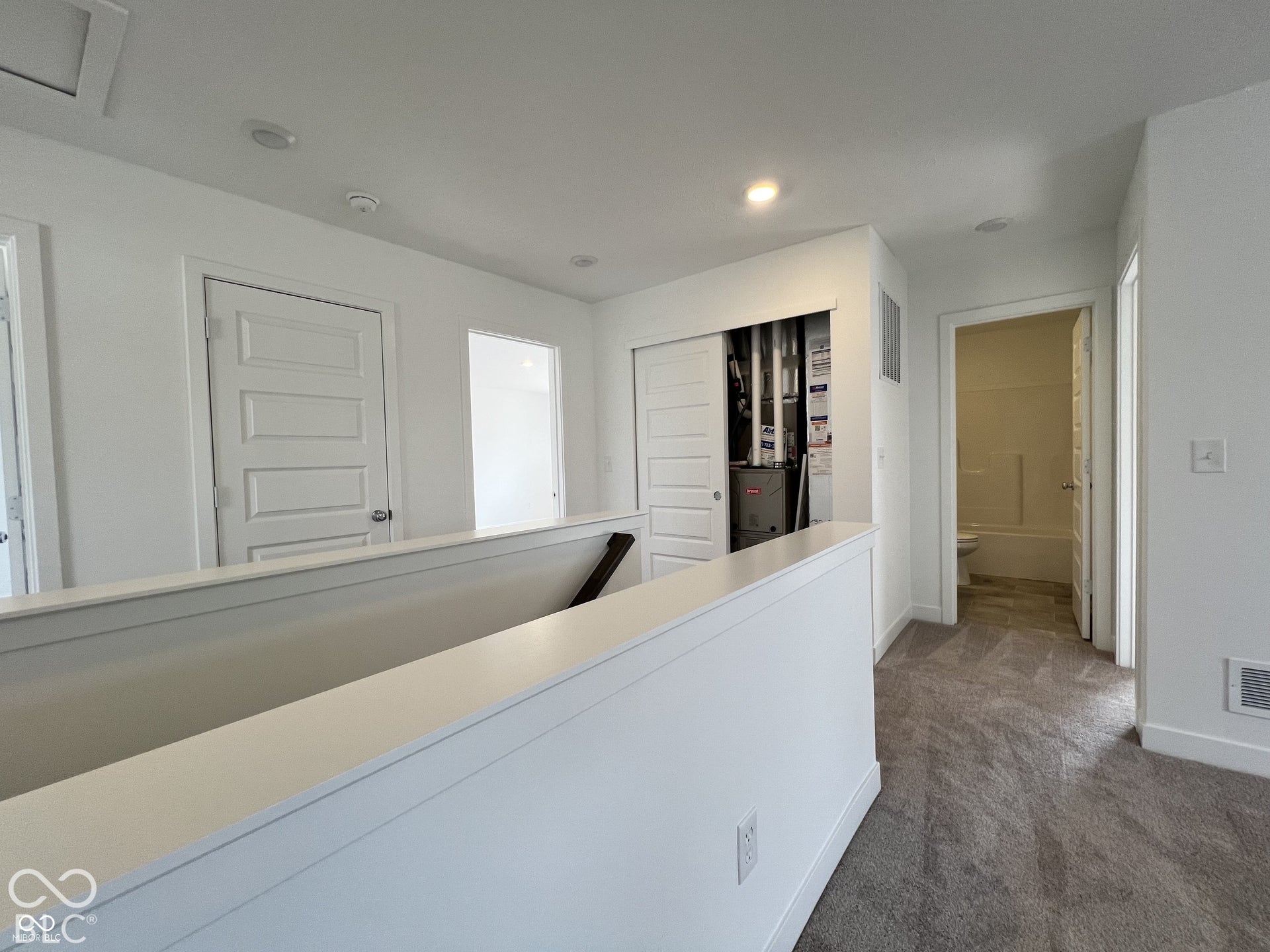 Upper-level hallway with neutral carpeting, recessed lighting, white paneled doors, and a utility closet with bifold doors