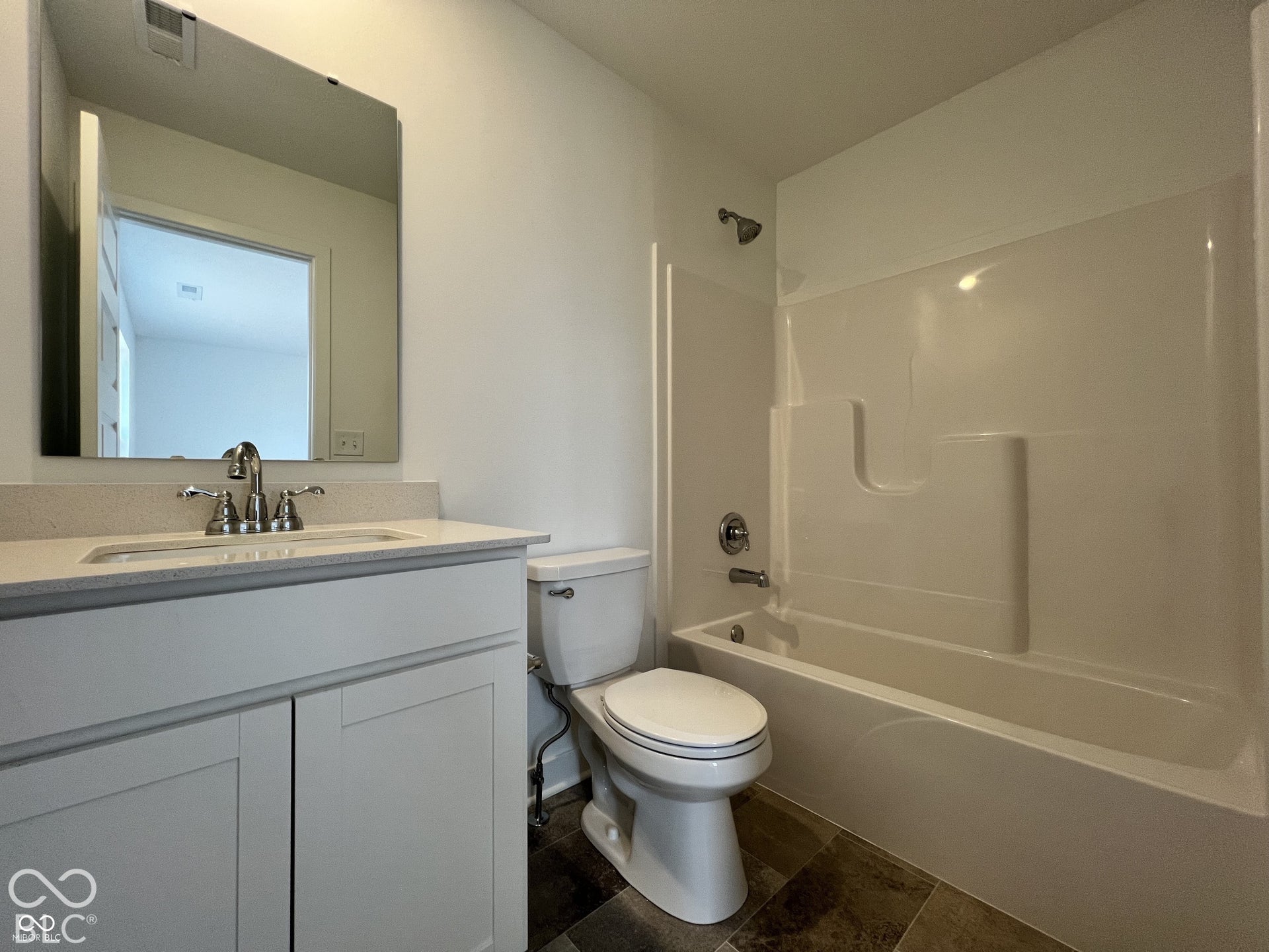 Bathroom featuring a single vanity with a light-colored countertop, an undermount sink, a chrome faucet, a wall-mounted mirror, and a white tub with shower