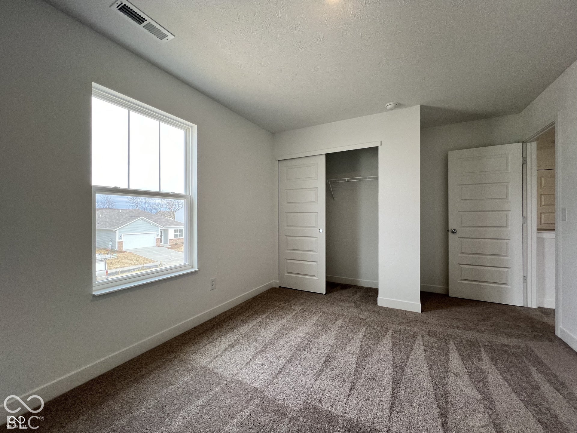 Carpeted room featuring a single window, white trim, and a built-in closet with sliding panel doors