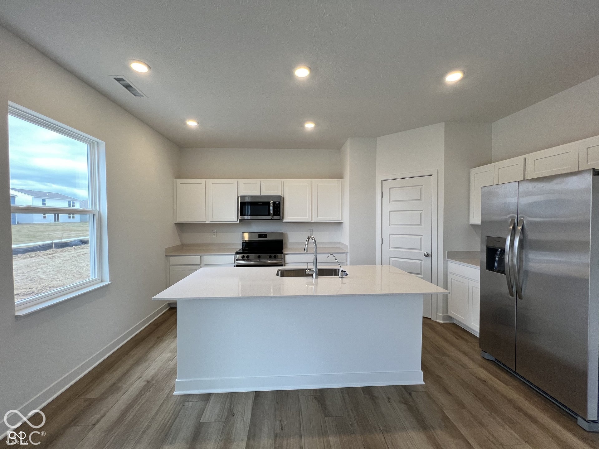 Kitchen featuring wood-finish flooring, white cabinetry, a central island with an integrated sink, stainless steel appliances, and recessed lighting