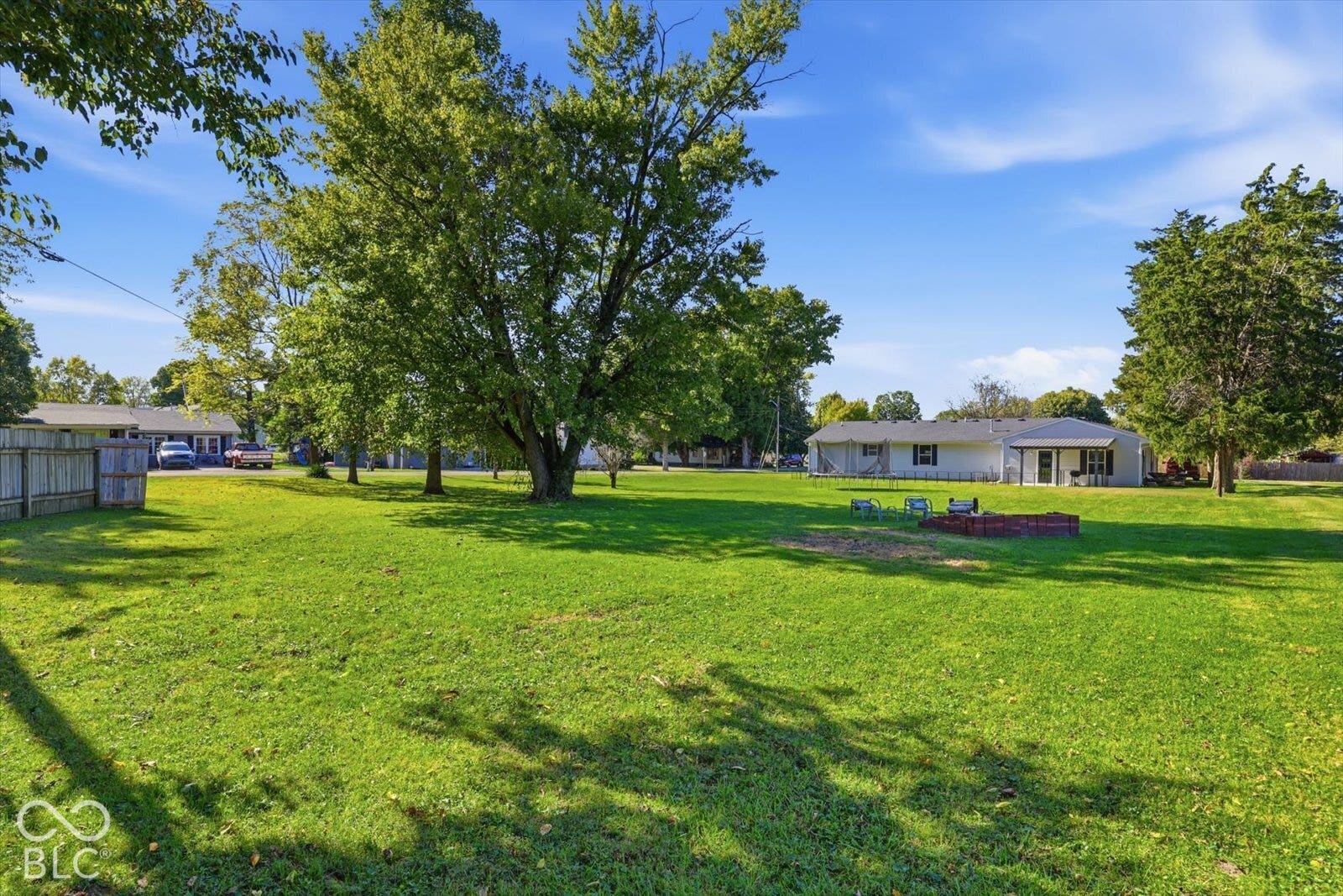 Expansive green lawn with mature trees and a brick-lined fire pit