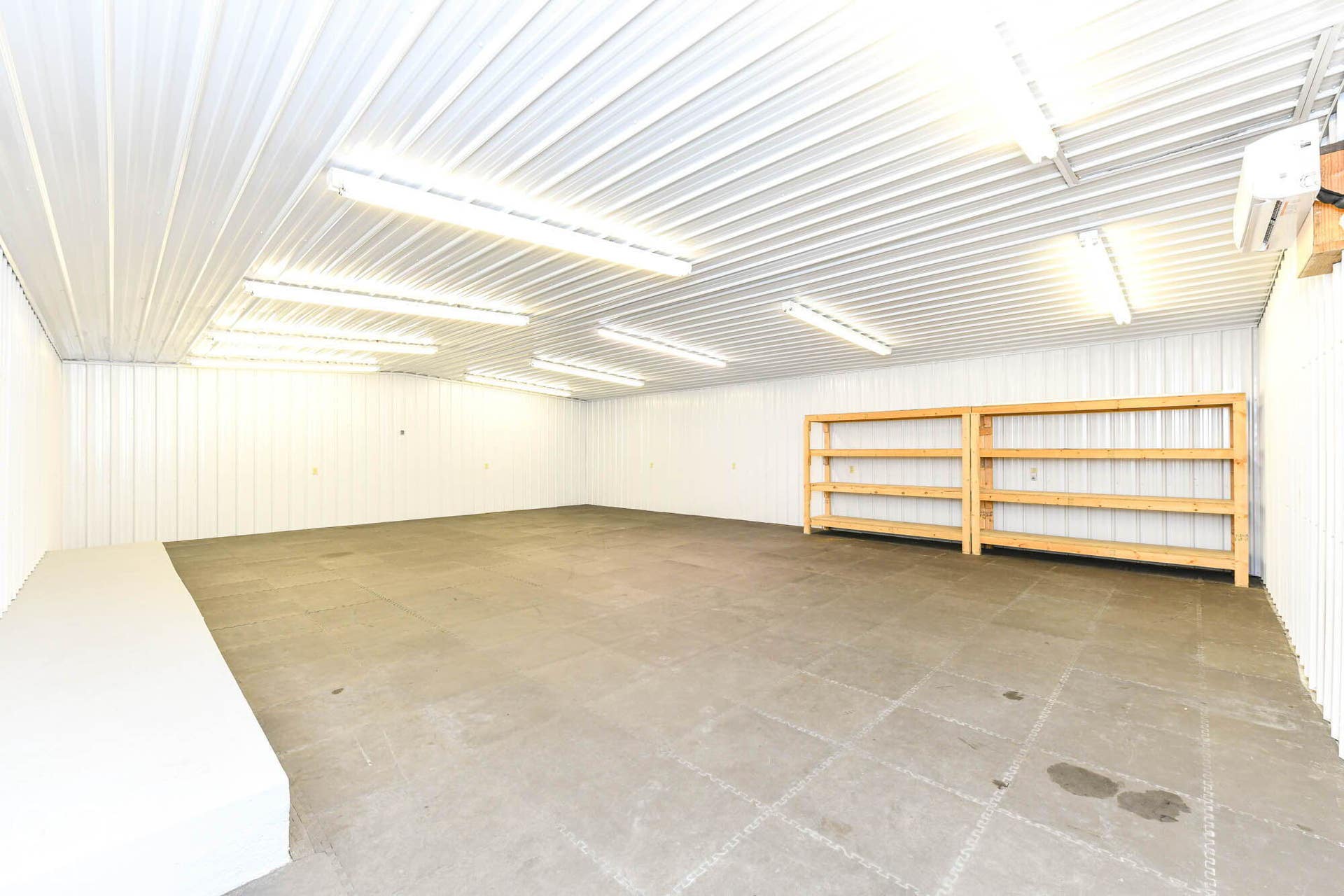 Expansive interior featuring an open layout, corrugated wall and ceiling panels, integrated fluorescent lighting, and built-in wood shelving units