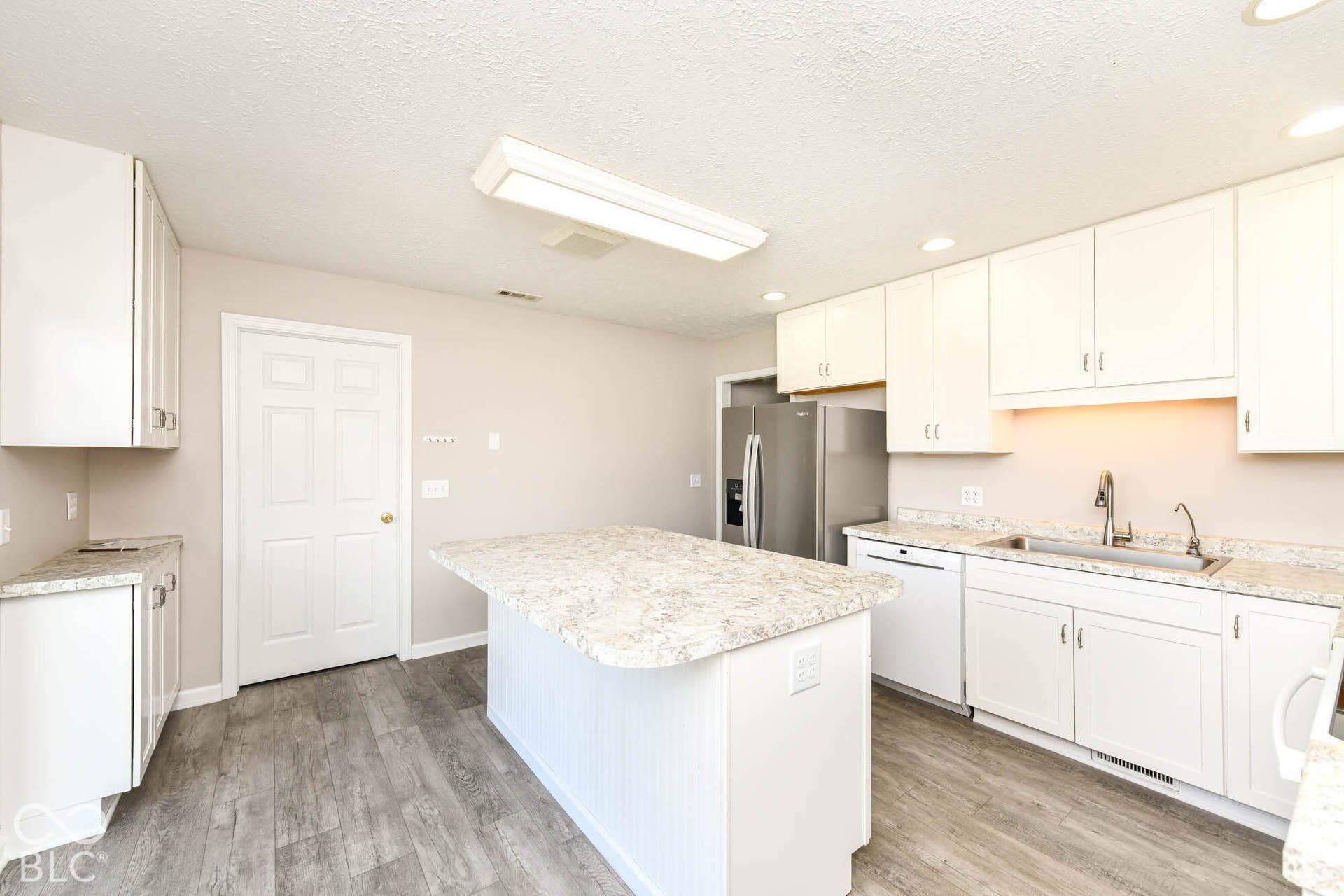 Kitchen featuring white cabinetry, light-toned countertops, wood-finish flooring, a center island, and stainless steel appliances