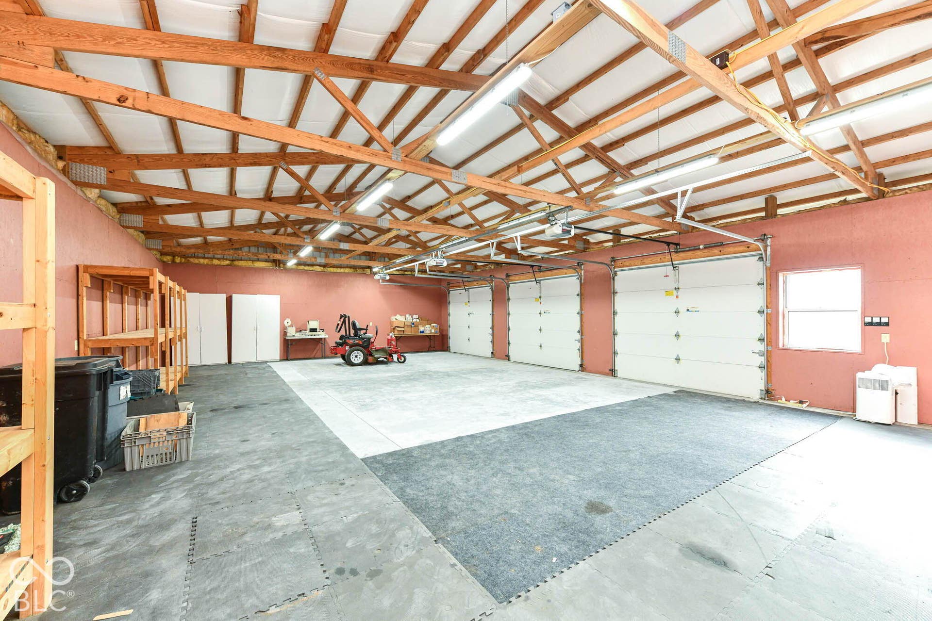 Spacious garage with exposed wood beam ceiling, multiple overhead doors, concrete flooring, and ample lighting