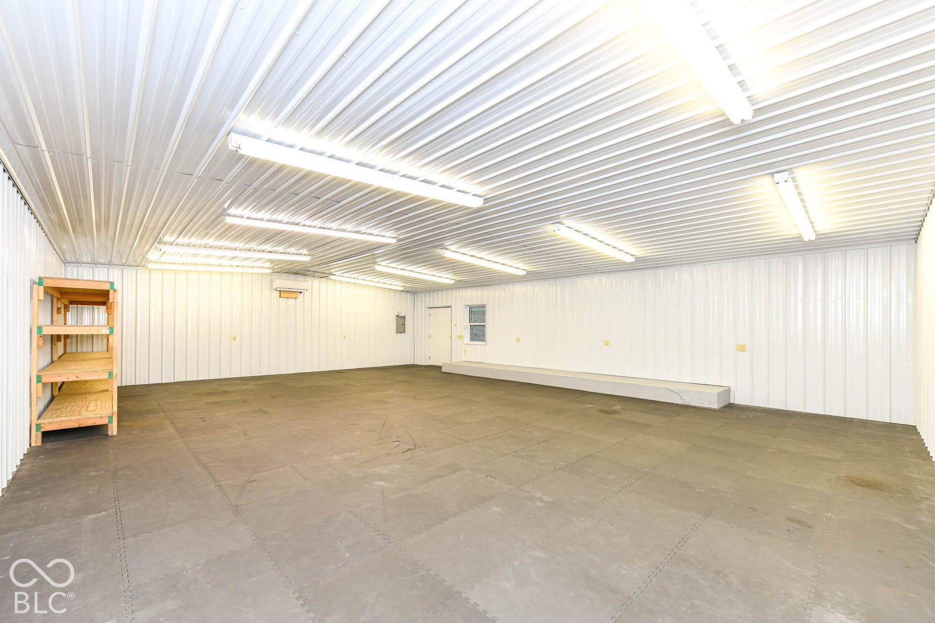 Expansive interior space featuring corrugated metal walls and ceiling, fluorescent lighting, and a durable floor