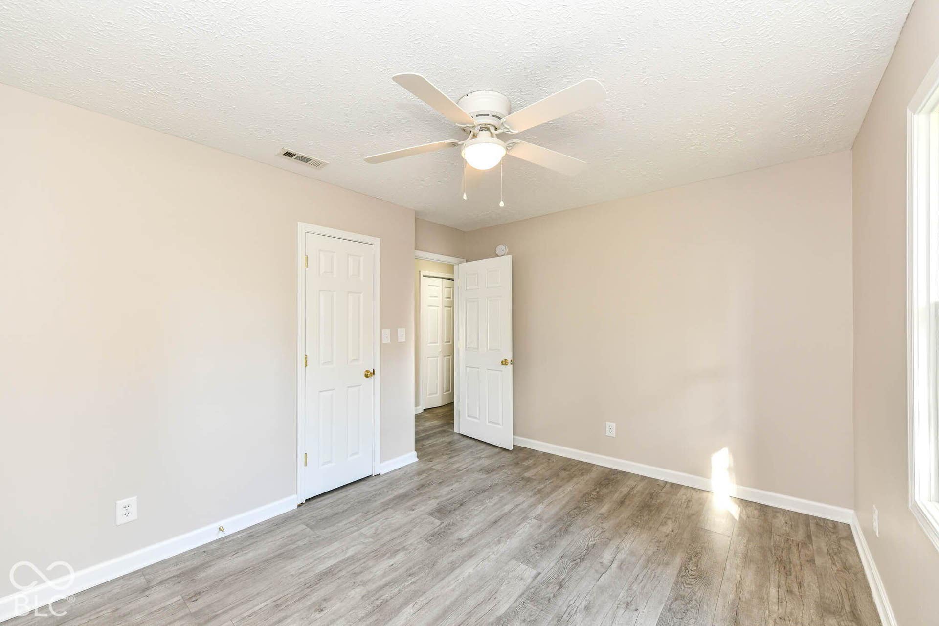 Light wood-finish flooring, neutral wall tones, white trim, and a ceiling fan with integrated lighting