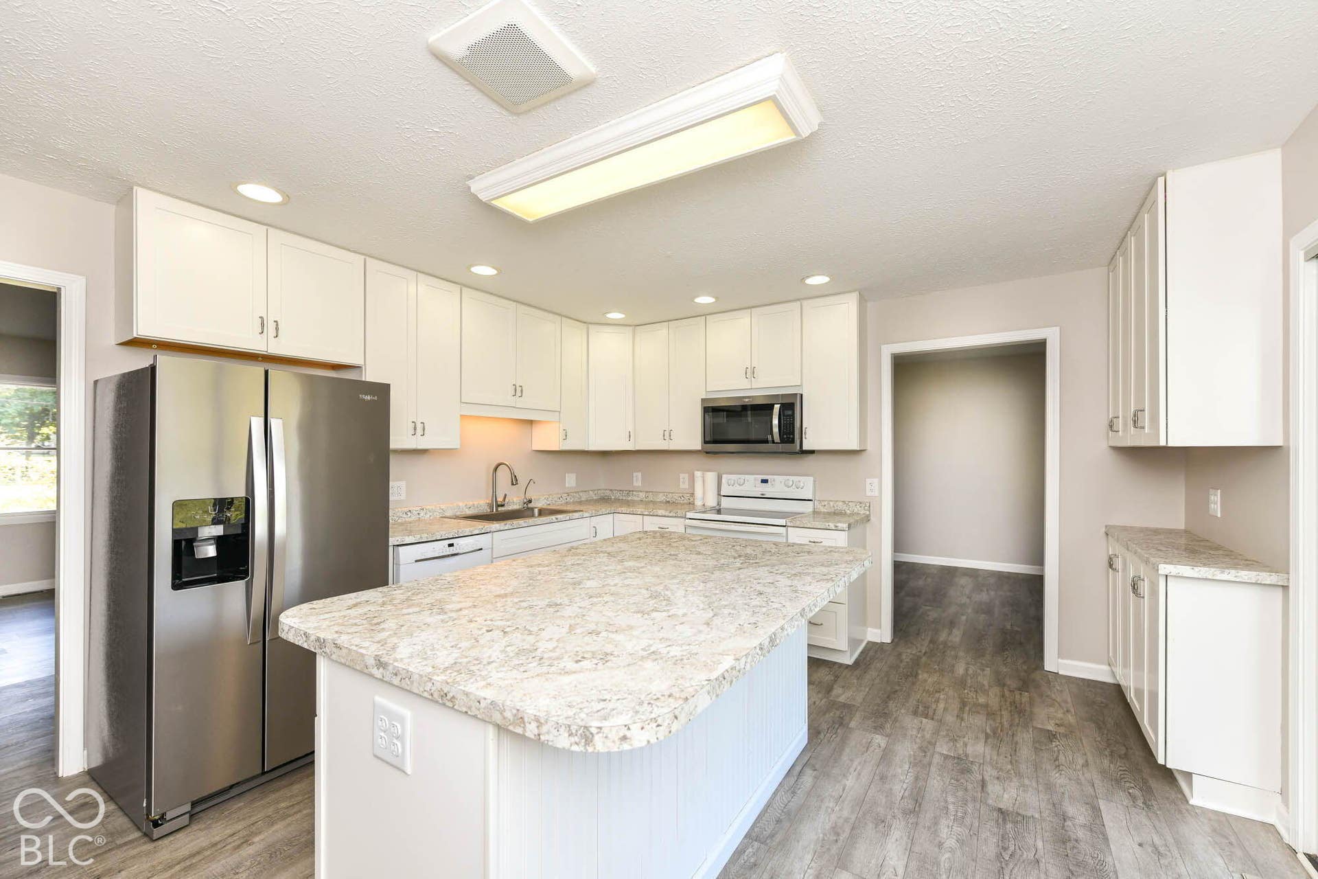 Kitchen featuring white cabinetry, light-toned countertops, stainless steel appliances, a center island, and wood-finish flooring