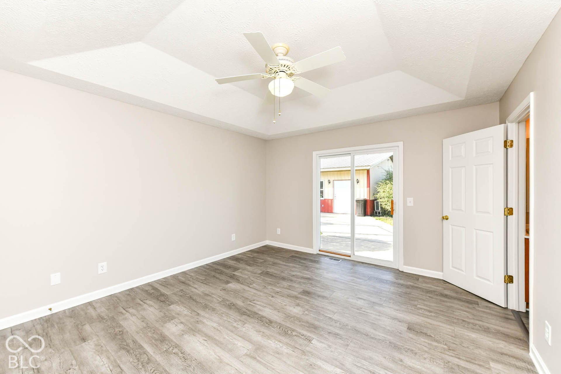 Tray ceiling with a ceiling fan, wood-finish flooring, sliding glass door, and a paneled interior door