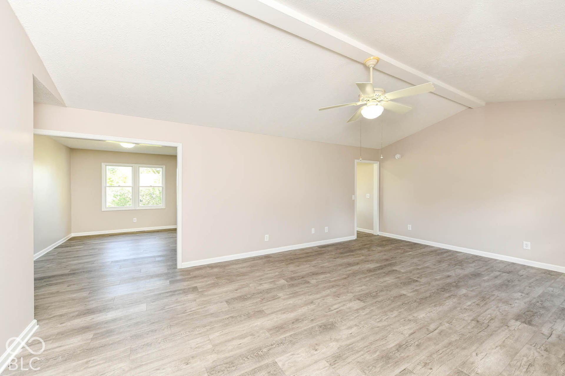 Vaulted ceiling with exposed beams, wood-finish flooring, ceiling fan with integrated lighting, and a wide entryway to an additional room