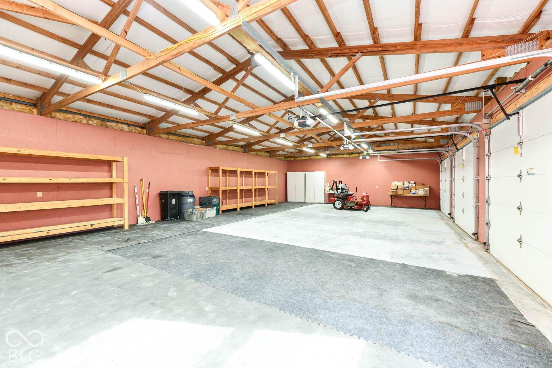 Spacious garage with exposed wooden beams, multiple overhead lights, and durable concrete flooring