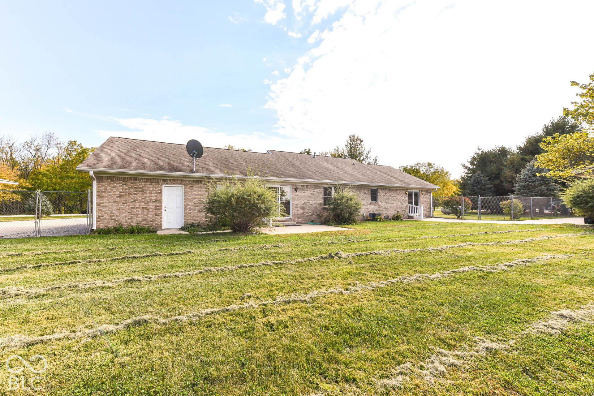Brick exterior, paved driveway, mature trees, chain-link fencing, rear patio