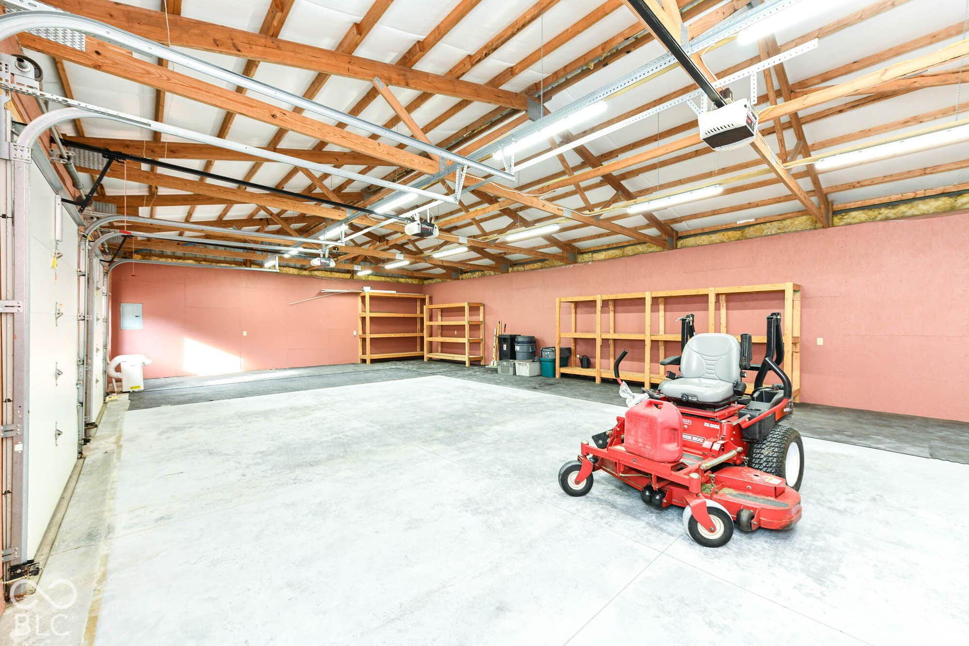 Spacious garage featuring a concrete floor, exposed wood beam ceiling, multiple fluorescent light fixtures, and a large overhead door