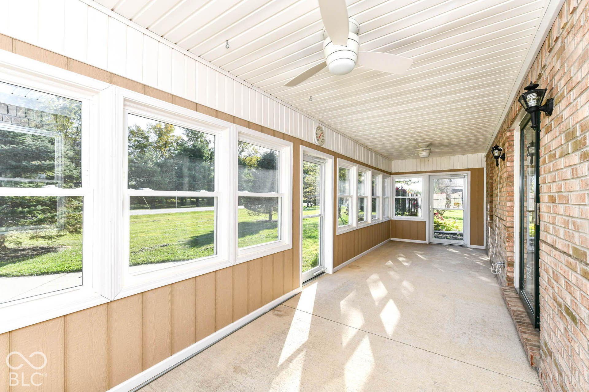 Enclosed porch with multiple windows, brick exterior wall, ceiling fans, and concrete flooring