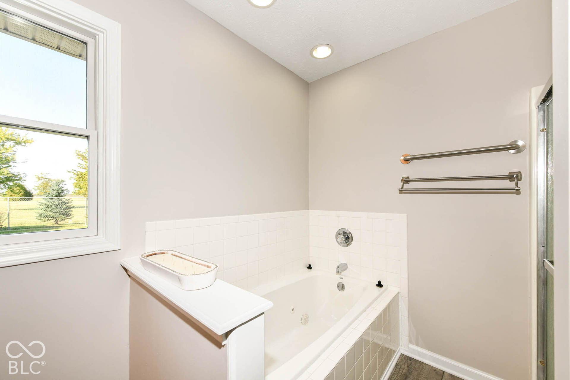 Jetted soaking tub with tile surround, recessed lighting, and a white-framed window