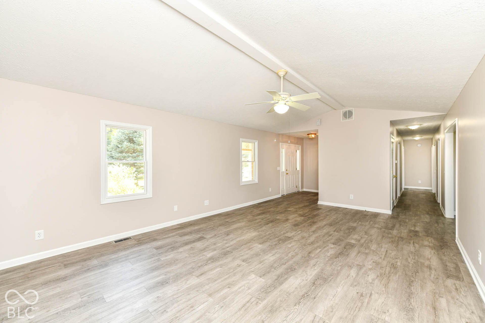 Spacious interior with wood-finish flooring, light neutral wall tones, multiple windows, and a ceiling fan with integrated lighting