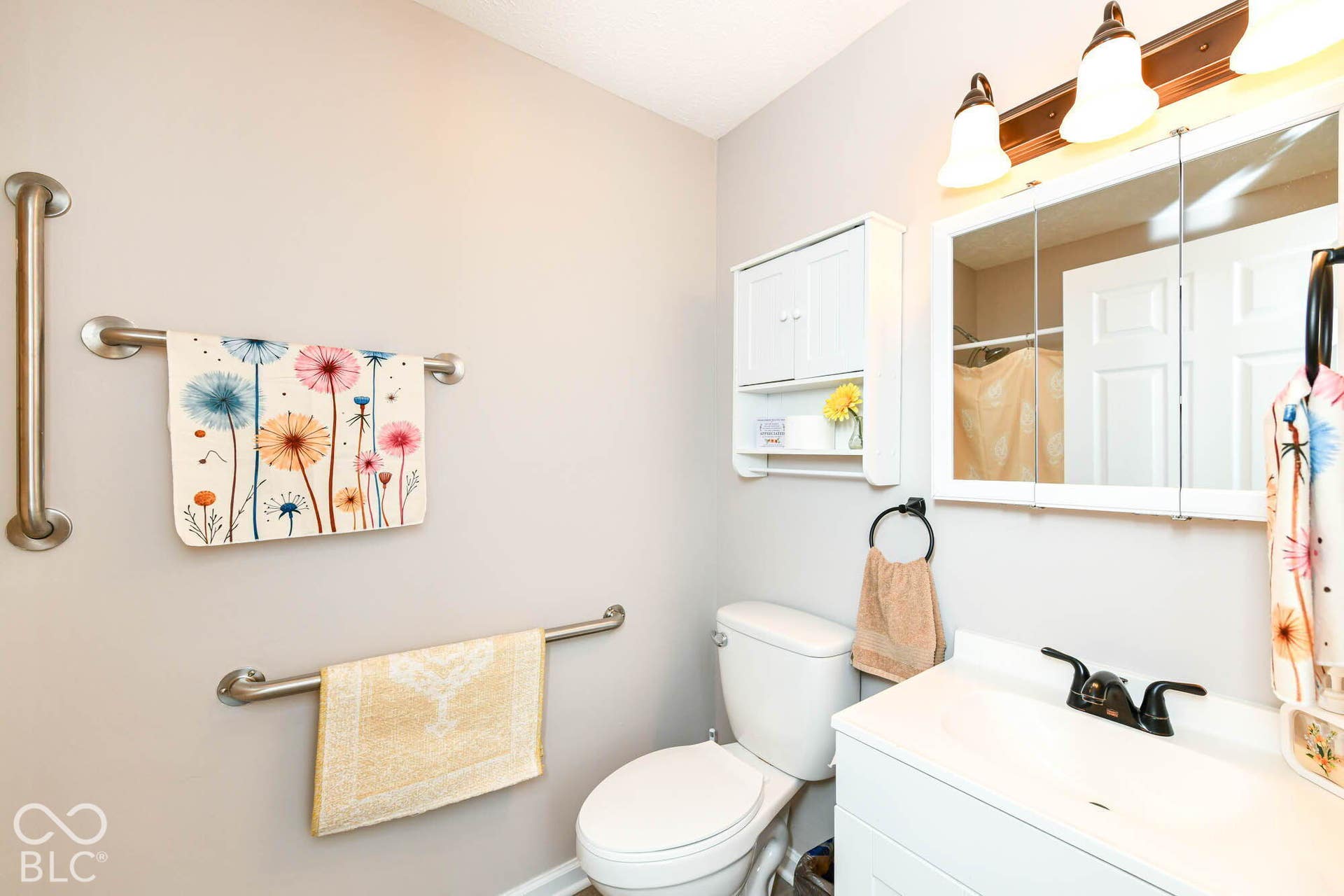 White vanity with integrated sink, mounted mirror with overhead lighting, and built-in wall cabinet storage