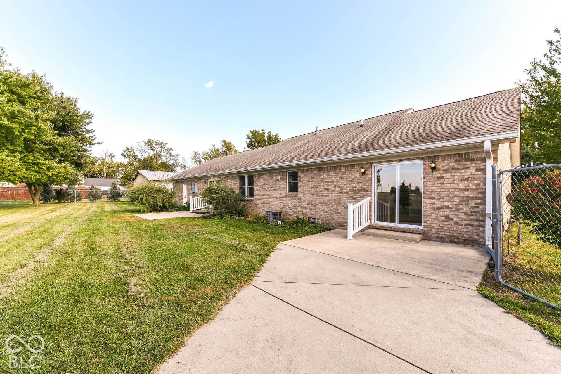 Brick exterior with a concrete patio, sliding glass door, and chain-link fencing