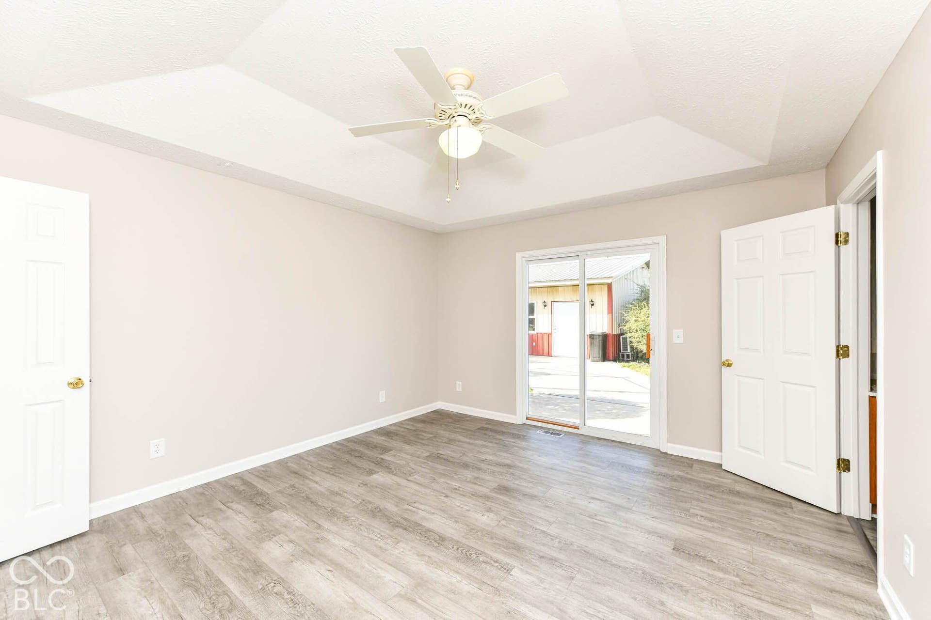Tray ceiling with a ceiling fan, light-toned wood-finish flooring, sliding glass door, and neutral wall paint