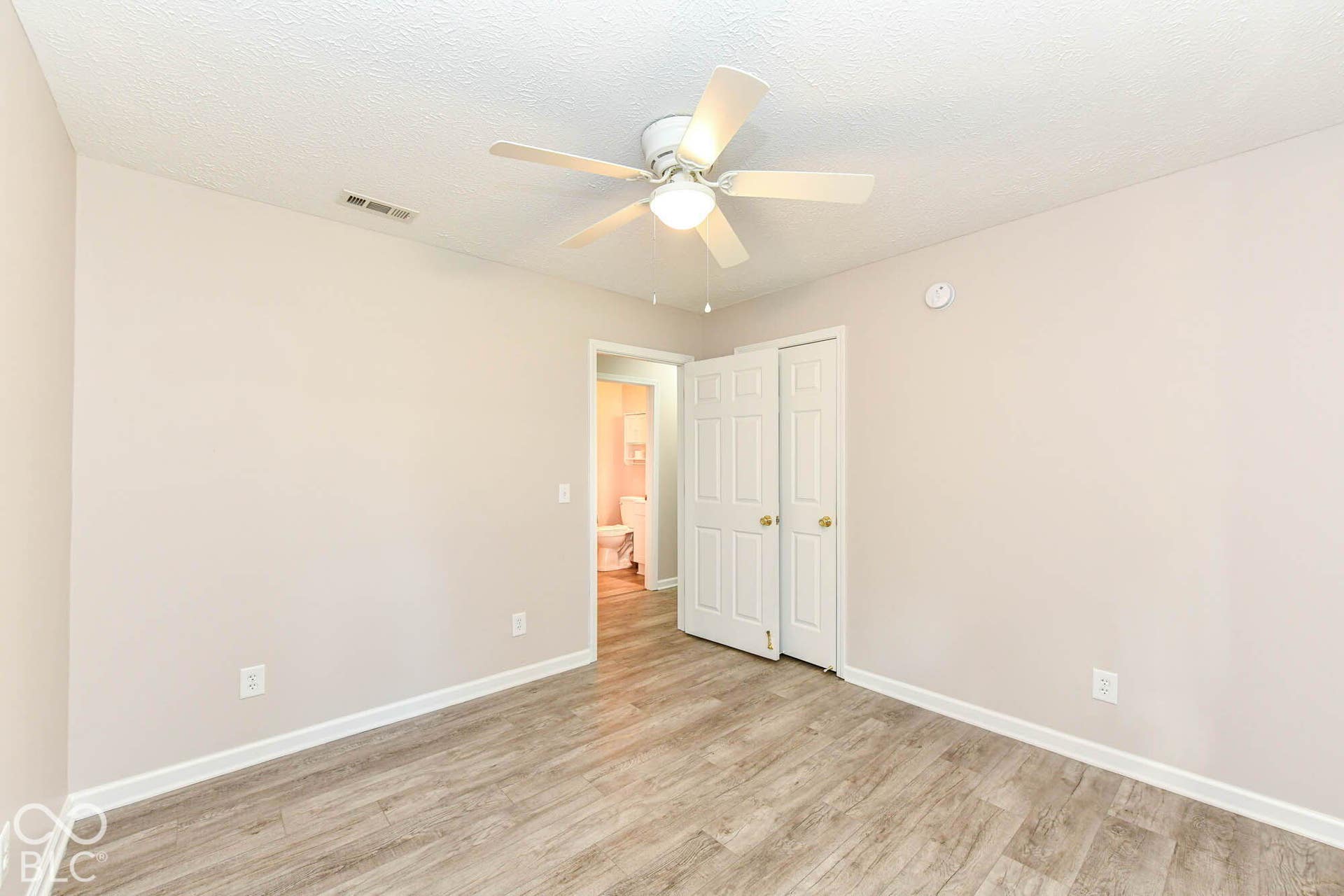 Wood-finish flooring, white bi-fold closet doors, ceiling fan with integrated lighting, and neutral wall paint
